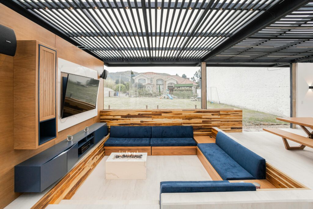 Contemporary outdoor living room featuring a cozy blue sofa, wooden accents, and glass wall.